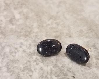 May include: A pair of oval-shaped stud earrings with a dark blue, sparkly finish.