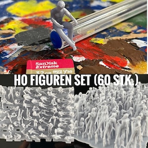 Puede incluir: Un conjunto de 60 figuras de plástico gris a escala HO en varias poses. Las figuras están dispuestas en una cuadrícula sobre un fondo blanco. El texto "HO FIGUREN SET (60 STK)" está impreso en letras negras sobre un fondo blanco.