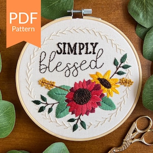 Puede incluir: Arte de bordado en aro con la frase "Simply Blessed" en escritura negra. El aro presenta un diseño floral con flores y hojas rojas, amarillas y verdes.