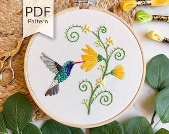 May include: Embroidered hummingbird and flower design in a wooden hoop. The hummingbird is teal, blue, and gray, with a red beak. The flower is yellow, and the embroidery is on white fabric. The text "PDF Pattern" is in the upper left corner.