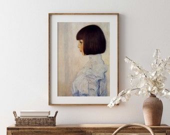 May include: A framed portrait of a young woman with dark hair, wearing a light blue and white dress. The portrait is set against a white background.