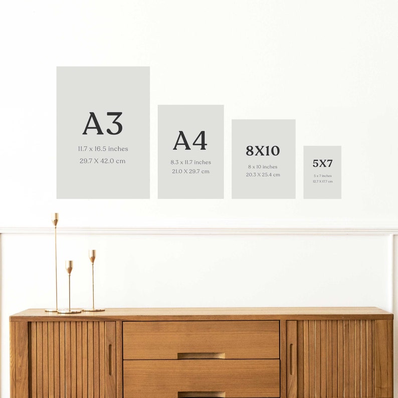 May include: A white wall with four different sized frames, each with a different size print. The frames are labelled with the print sizes: A3, A4, 8x10, and 5x7. The frames are all white and have a simple, modern design. The frames are hanging on the wall above a wooden dresser.