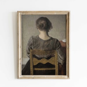 May include: A framed painting depicting a woman seated in a chair, with her back to the viewer. She is wearing a grey dress and has her hair tied back. The chair is wooden and has a simple design.