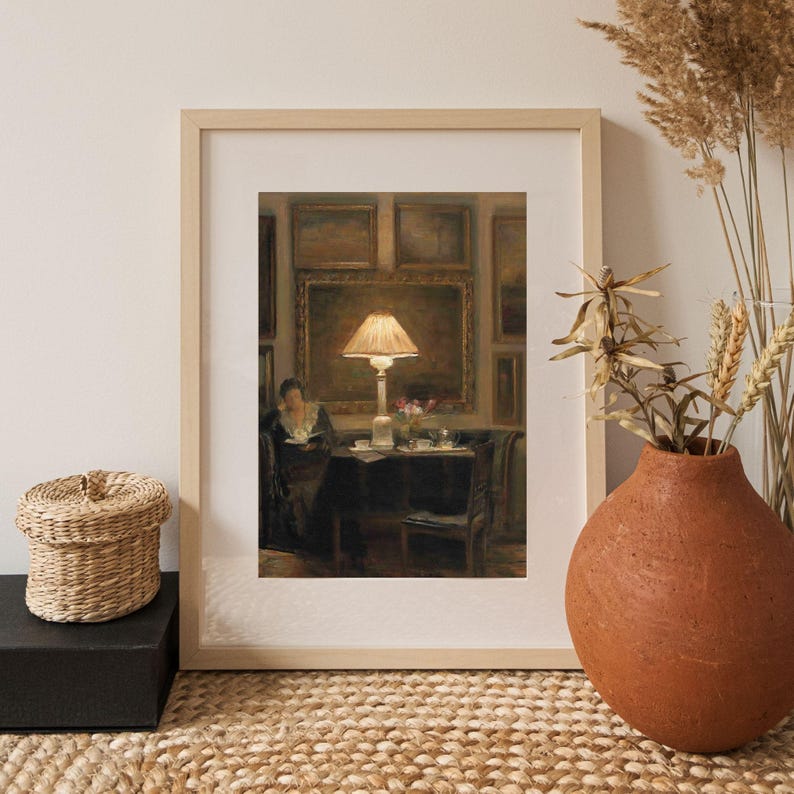 Vintage art print of a cozy interior scene with a glowing lamp, woman reading by a table, surrounded by framed paintings, flowers, and tea cups