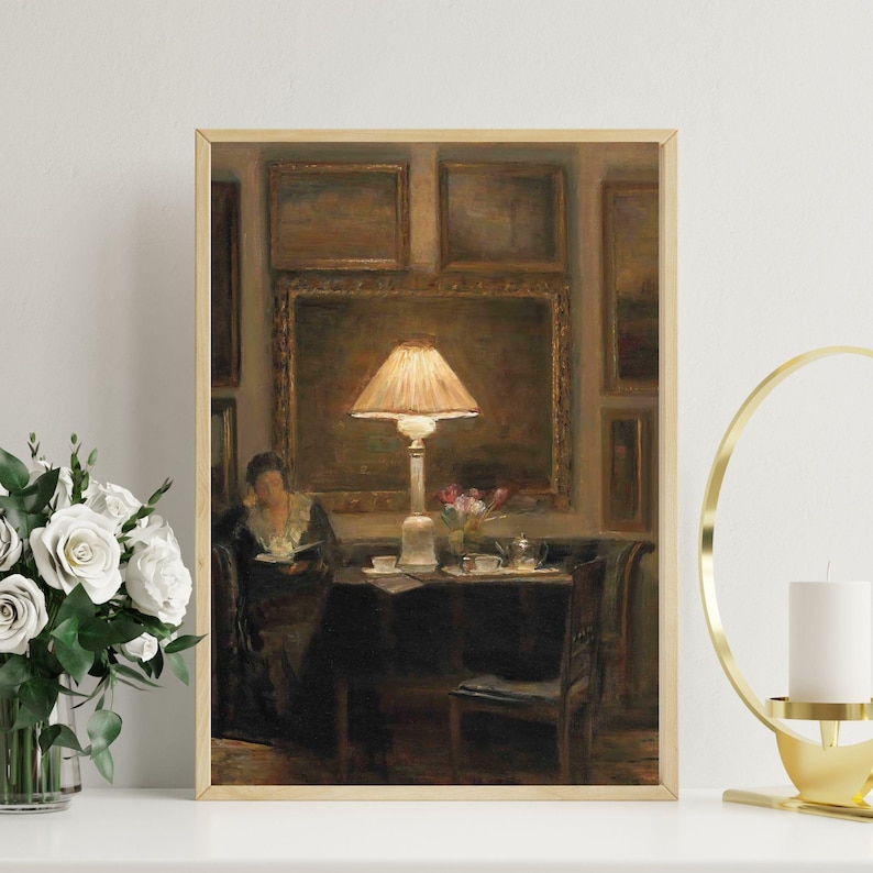 Vintage art print of a cozy interior scene with a glowing lamp, woman reading by a table, surrounded by framed paintings, flowers, and tea cups