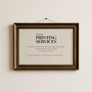 May include: A rectangular framed print with the text "Custom PRINTING SERVICES". The frame is a dark, ornate gold color. The print offers archival inks and custom sizes up to A2. The print is hanging on a white wall.