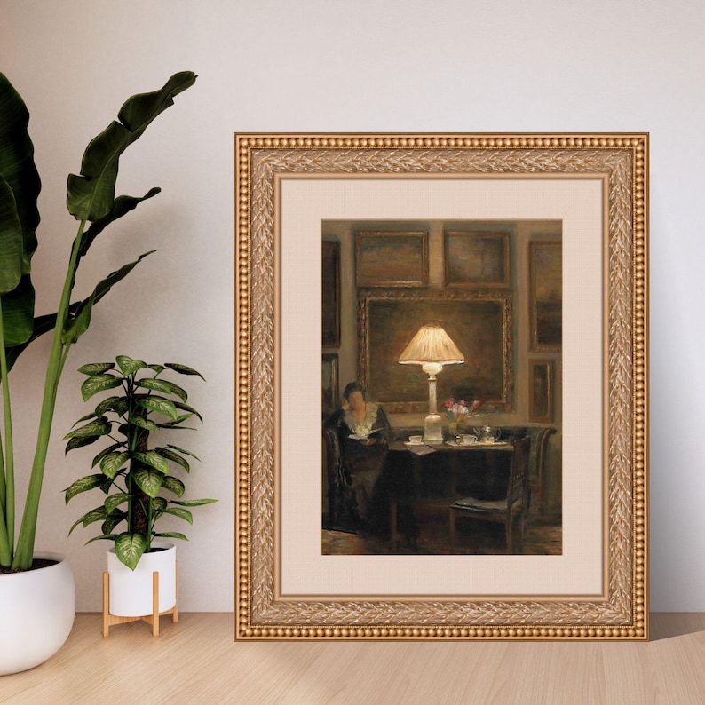 Vintage art print of a cozy interior scene with a glowing lamp, woman reading by a table, surrounded by framed paintings, flowers, and tea cups
