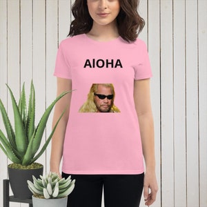 Pode incluir: Camiseta rosa com um gráfico preto de um homem com óculos de sol e o texto "AIOHA" impresso na frente.
