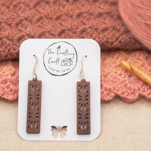May include: A pair of brown wooden earrings with intricate cutouts, hanging from silver hooks. The earrings are displayed on a white card with the text "The Crafting Croft Isle of Skye".