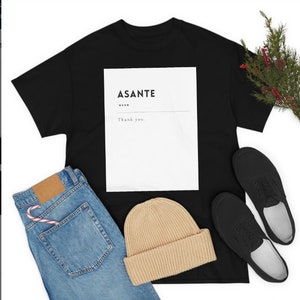 May include: Black t-shirt with a white rectangle featuring the text "ASANTE" and "Thank you."  The shirt is laid flat on a white surface with a pair of black shoes, a beanie, and blue jeans.