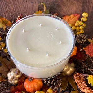May include: A large, clear glass jar candle with a white wax base and multiple wicks. The candle is surrounded by fall-themed decorations, including faux leaves, gourds, and berries.
