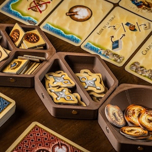 K&ouml;nnte beinhalten: Ein h&ouml;lzerner Spielorganisator mit F&auml;chern zur Aufbewahrung von Spielsteinen. Der Organisator hat eine sechseckige Form und ist aus dunkelbraunem Holz gefertigt. Die F&auml;cher sind mit verschiedenen Spielsteinen gef&uuml;llt, darunter kleine Holzmarker, Karten und M&uuml;nzen. Der Organisator steht auf einem Holztisch.