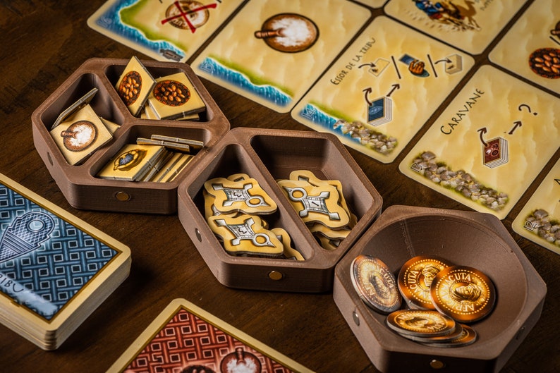 K&ouml;nnte beinhalten: Ein h&ouml;lzerner Spielorganisator mit F&auml;chern zur Aufbewahrung von Spielsteinen. Der Organisator hat eine sechseckige Form und ist aus dunkelbraunem Holz gefertigt. Die F&auml;cher sind mit verschiedenen Spielsteinen gef&uuml;llt, darunter kleine Holzmarker, Karten und M&uuml;nzen. Der Organisator steht auf einem Holztisch.