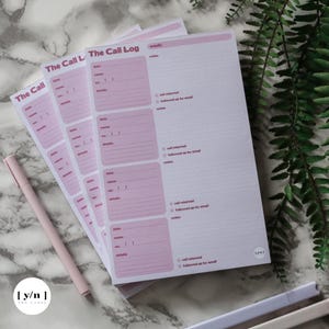 Op de afbeelding: Roze en witte notitieblokken met de tekst "The Call Log" en velden om beldetails vast te leggen. Een roze pen ligt naast de notitieblokken. Het merklogo "[y/n] THE LABEL" is zichtbaar.