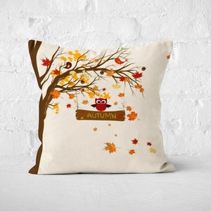 Pu&ograve; includere: Un cuscino decorativo con sfondo bianco che presenta un albero marrone con foglie arancioni e gialle. Un gufo &egrave; appollaiato su un ramo con un cartello che dice "Autunno".
