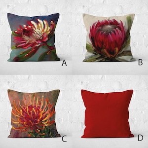 Op de afbeelding: Vier vierkante kussens. Drie kussens hebben bloemmotieven in tinten rood, oranje en groen. Het vierde kussen is effen rood. De kussens zijn geplaatst tegen een witte bakstenen muur.