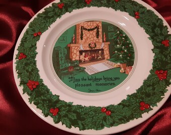 May include: A white ceramic Christmas plate with a green holly border and red berries. The center of the plate features a festive scene of a fireplace with stockings, a Christmas tree, and a message that reads "May the holidays bring you pleasant memories."