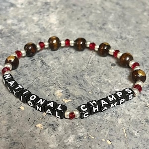 Könnte beinhalten: Ein schwarzes und rotes Perlenarmband mit den Worten "NATIONAL CHAMPS" in weißen Buchstaben auf schwarzen Perlen.