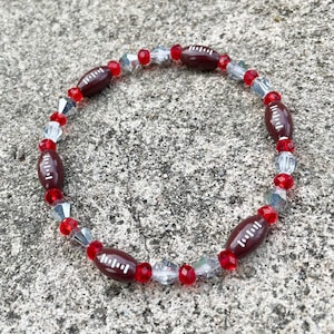 May include: A red and clear beaded bracelet with brown football-shaped beads.