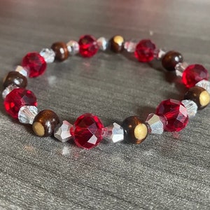 Könnte beinhalten: Ein rotes und braunes Perlenarmband mit silbernen Akzenten. Das Armband besteht aus runden Perlen und hat ein schlichtes Design.