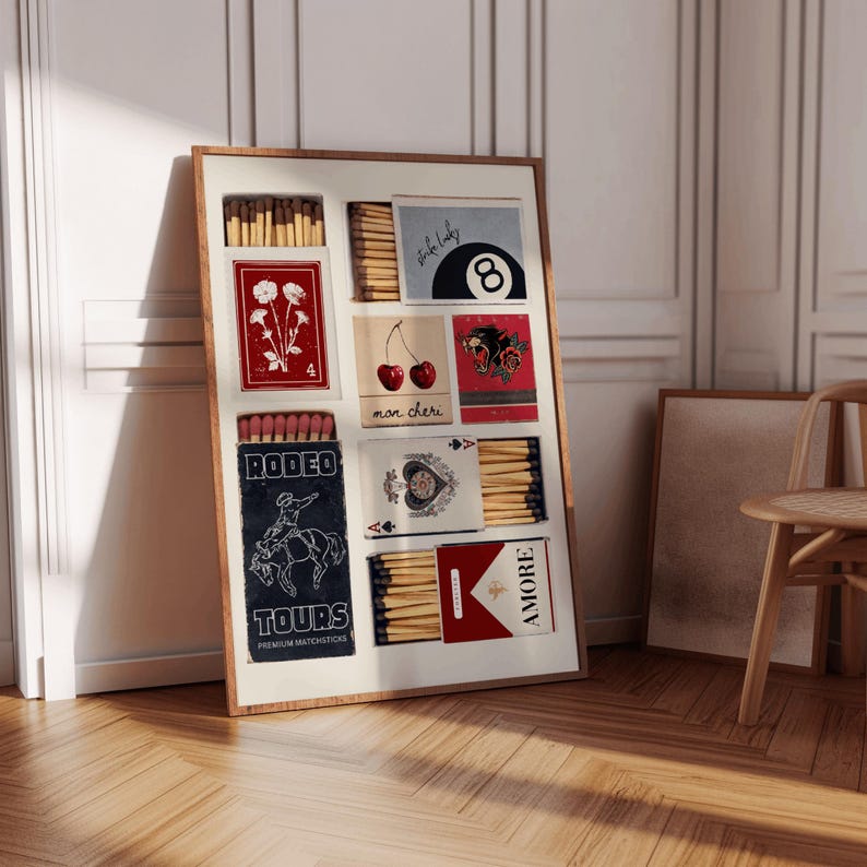 May include: A framed collage of matchboxes with various designs. The matchboxes feature images of flowers, cherries, a playing card, a cowboy riding a horse, a black panther, and a pool ball. The matchboxes are arranged in a grid pattern and have a vintage aesthetic.
