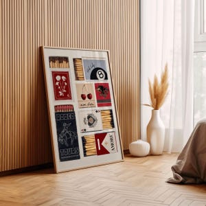 May include: A framed collage of matchbox labels with various designs, including cherries, a cowboy on a horse, a playing card, a pool ball, and flowers. The labels are in red, blue, and white with black text.