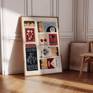 May include: A framed collage of matchboxes with various designs, including a red box with a flower, a red box with cherries, a red box with a panther, a blue box with a cowboy riding a horse, a blue box with a playing card, and a red box with the word "AMORE".