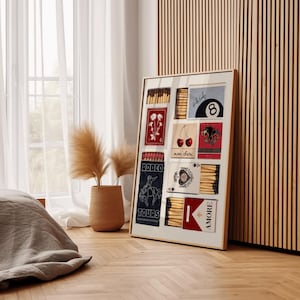 May include: A framed collage of matchboxes with various designs, including a cowboy riding a horse, a heart with playing cards, cherries, and a red flower. The matchboxes are arranged in a grid pattern and have a white background. The frame is gold and has a white mat.