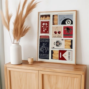 May include: A framed collage of vintage matchbox labels with various designs, including a cowboy riding a horse, a playing card, cherries, a skull, and a pool ball. The labels are arranged in a grid pattern and have a vintage aesthetic.