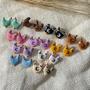 May include: A set of 18 colorful ceramic chicken earrings. Each earring features a different color and design, including pink, purple, blue, yellow, orange, brown, and black. The earrings are all shaped like chickens with a small '3' painted on each one.