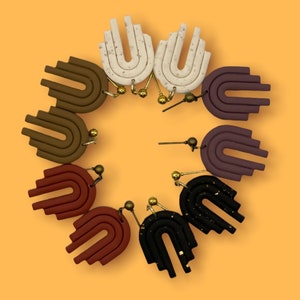 May include: A set of eight pairs of handmade polymer clay earrings. The earrings are shaped like arches with multiple layers. The earrings are in various colors, including brown, purple, black, and white.