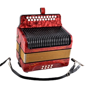 Op de afbeelding: Een rode parelmoerkleurige Hohner-accordeon met een zwart balggedeelte, een beige stoffen middenstuk en witte ronde knoppen. Het instrument is voorzien van een zwarte lederen schouderriem met metalen gespen aan de zijkanten bevestigd.