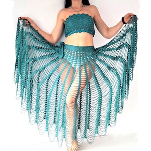 May include: A teal crochet two-piece set consisting of a strapless tube top with a scalloped edge and a matching floor-length skirt. The skirt features an intricate open-work design with long, dangling vertical fringe strands in a fan-like pattern.