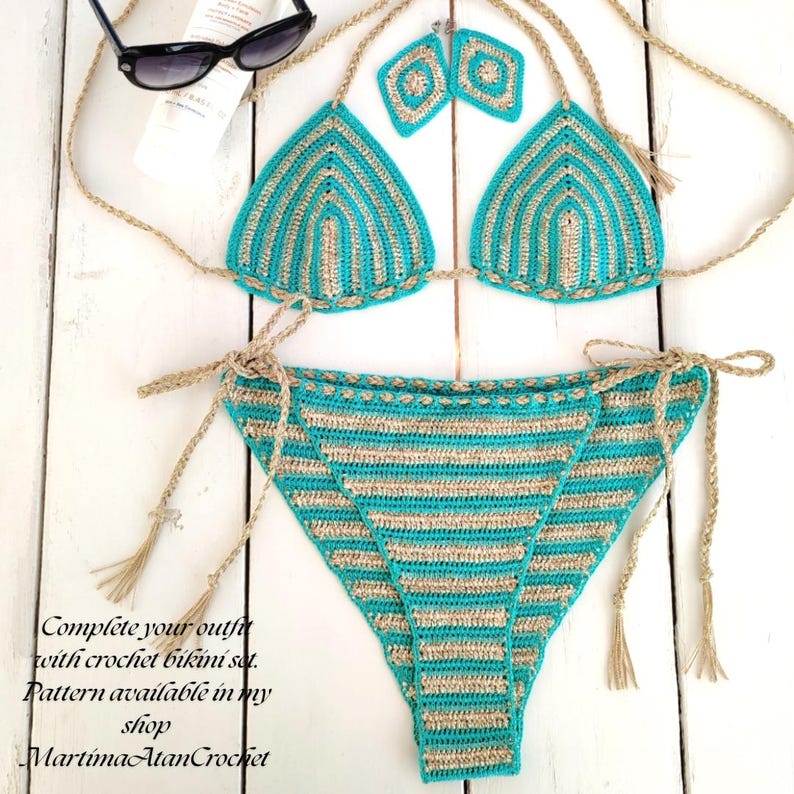 May include: A two-piece crochet bikini set featuring alternating horizontal stripes of turquoise and metallic gold yarn. The top consists of two triangular cups with matching diamond-shaped earrings, while the bottom has side ties with tassels.