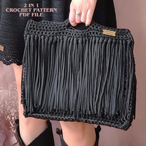 May include: A black crochet handbag featuring long fringe detailing across the front and a small rectangular wooden label with the text Martima Hand Made. The text 2 IN 1 CROCHET PATTERN PDF FILE is visible in the upper left corner of the image.