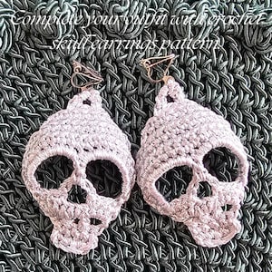 Puede incluir: Un par de pendientes de calavera de ganchillo en color rosa claro con cierres de clip met&aacute;licos. El texto "Complete your outfit with crochet skull earrings pattern" es visible en la parte superior. Los pendientes muestran puntadas detalladas.