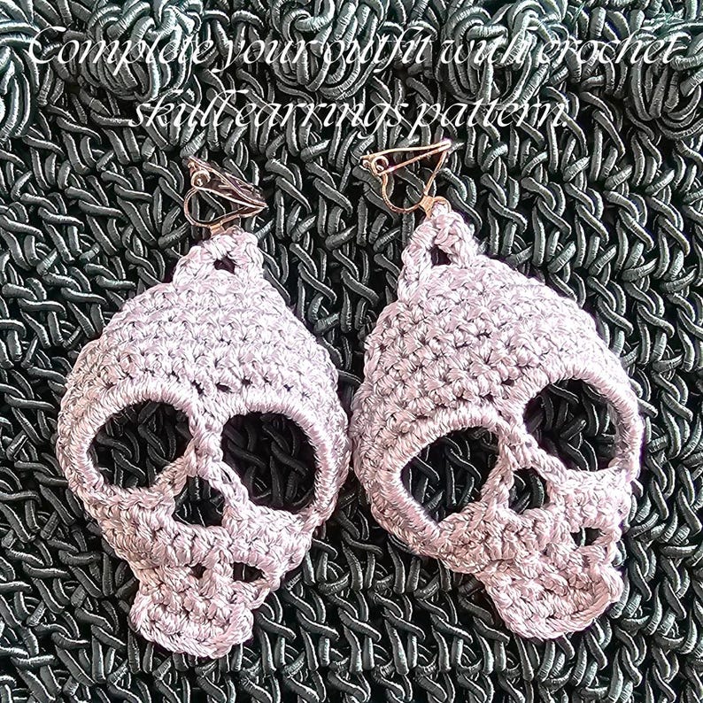 Puede incluir: Un par de pendientes de calavera de ganchillo en color rosa claro con cierres de clip met&aacute;licos. El texto "Complete your outfit with crochet skull earrings pattern" es visible en la parte superior. Los pendientes muestran puntadas detalladas.