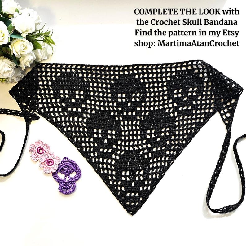 K&ouml;nnte beinhalten: Ein schwarzes, dreieckiges H&auml;kel-Bandana mit Totenkopfmuster und Bindeb&auml;ndern. Daneben liegen zwei kleine rosa H&auml;kelblumen und ein violettes H&auml;kel-Totenkopfmotiv. Der Text lautet: COMPLETE THE LOOK with the Crochet Skull Bandana.