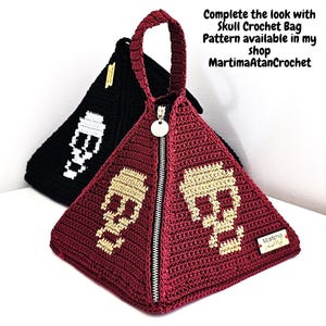 Puede incluir: Dos bolsos de ganchillo en forma de pir&aacute;mide, uno burdeos y otro negro, cada uno con un motivo de calavera. El bolso burdeos tiene una cremallera plateada, una etiqueta met&aacute;lica redonda y una etiqueta de marca rectangular. El texto dice: Complete the look with Skull Crochet Bag Pattern available in my shop MartimaAtanCrochet.