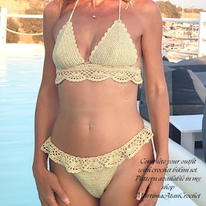 May include: A pale yellow crochet bikini set featuring a triangle top with scalloped edges and matching bottoms with a ruffled trim. The text on the image reads: Complete your outfit with crochet bikini set. Pattern available in my shop MartimaAtanCrochet.