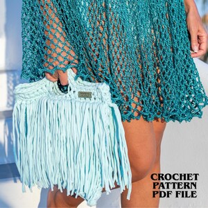 May include: A light blue crochet handbag featuring long fringe detailing and a small rectangular label with the text Marima Hand Made. The bag is held against a teal green crochet net cover-up. The image includes the text CROCHET PATTERN PDF FILE.