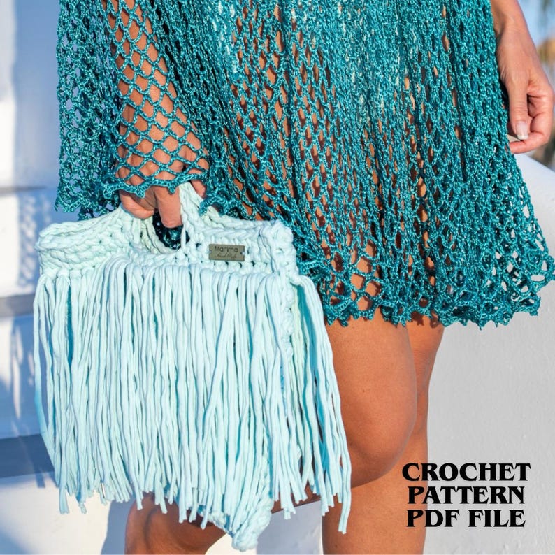 May include: A light blue crochet handbag featuring long fringe detailing and a small rectangular label with the text Marima Hand Made. The bag is held against a teal green crochet net cover-up. The image includes the text CROCHET PATTERN PDF FILE.