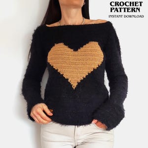 May include: A black long-sleeved sweater with a fuzzy texture and a large, centered tan heart motif. The text CROCHET PATTERN INSTANT DOWNLOAD is visible in the upper right corner. The sweater features a wide neckline and long sleeves.