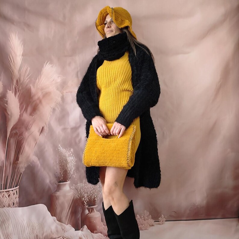 K&ouml;nnte beinhalten: Eine Frau tr&auml;gt ein senfgelbes Kleid, eine schwarze Strickjacke und schwarze Stiefel. Sie tr&auml;gt auch einen passenden senfgelben Hut und eine senfgelbe Handtasche. Das Outfit ist vor einem weichen rosa Hintergrund.