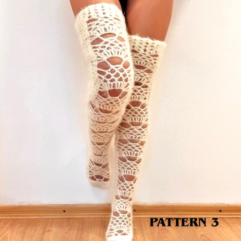 May include: A pair of off-white, over-the-knee crochet stockings featuring an intricate, open-work lace pattern with a fuzzy, textured yarn finish. The stockings extend from the feet up to the mid-thigh, displaying a repeating geometric design.
