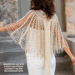 May include: A cream-colored crochet cape featuring an open, net-like stitch pattern with long, dangling fringe accents. The text on the image reads: Complete the look with Crochte Cape Pattern available in my shop MartimaAtanCrochet.