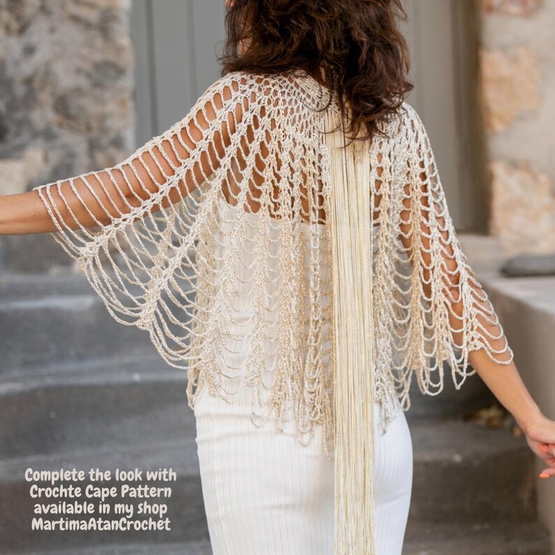 May include: A cream-colored crochet cape featuring an open, net-like stitch pattern with long, dangling fringe accents. The text on the image reads: Complete the look with Crochte Cape Pattern available in my shop MartimaAtanCrochet.