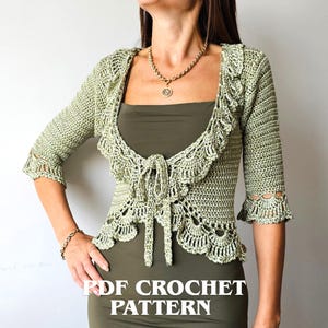 May include: A light sage green crochet bolero featuring three-quarter length sleeves with decorative scalloped cuffs, a ruffled collar, and a front tie closure. The text INSTANT DOWNLOAD and PDF CROCHET PATTERN is visible on the image.