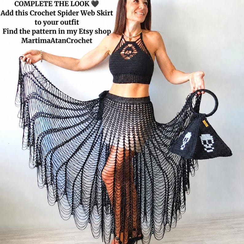 May include: A black crochet halter top and a matching black crochet spider web skirt with long fringe. A black pyramid-shaped crochet handbag with white skull motifs and a circular handle is held to the side. Text reads: COMPLETE THE LOOK. Add this Crochet Spider Web Skirt to your outfit. Find the pattern in my Etsy shop MartimaAtanCrochet.