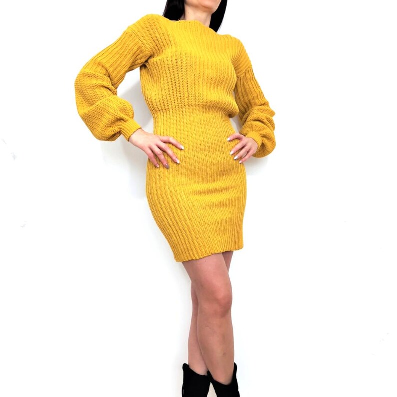 K&ouml;nnte beinhalten: Senfgelbes Strickkleid mit langen &Auml;rmeln und figurbetonter Silhouette. Das Kleid hat einen runden Ausschnitt und eine gerippte Struktur. Die &Auml;rmel haben eine leichte Ballonform am Oberarm. Das Kleid ist knielang.